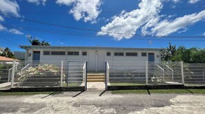 A building with a white exterior, a front door, and a small set of stairs leading up to the entrance. There are two metal gates in front of the building.