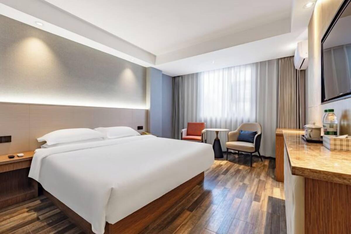 Habitación de hotel con una cama grande, un escritorio, una silla, un televisor y una ventana con cortinas.