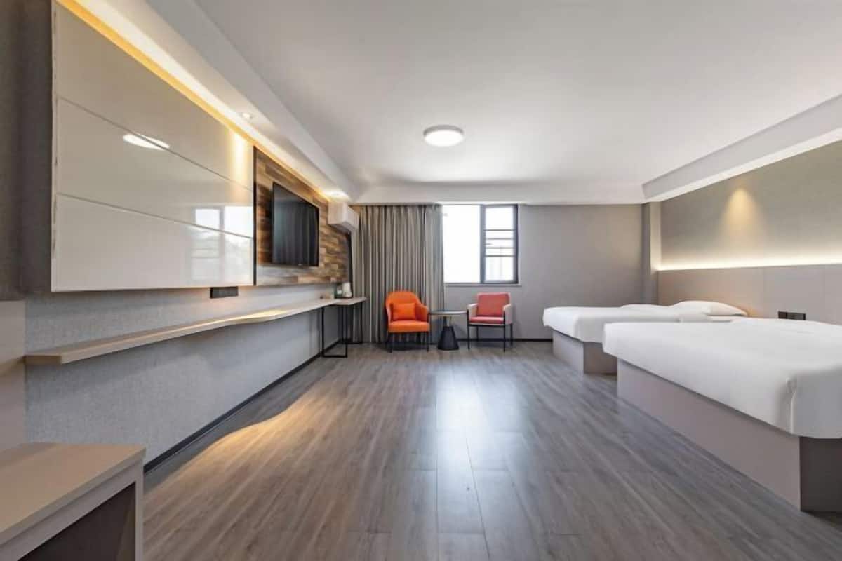 Una habitación de hotel con televisión de pantalla plana en la pared, un sofá, dos camas individuales, una mesita y una silla.
