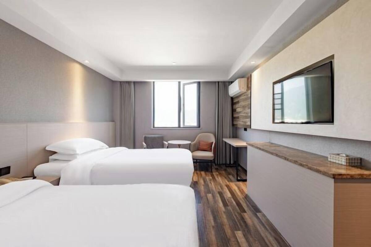 Habitación de hotel con dos camas, un escritorio, un televisor y una ventana.