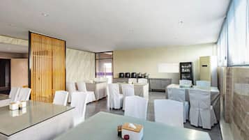 A modern hotel room with a dining area, a kitchen, and a large window.