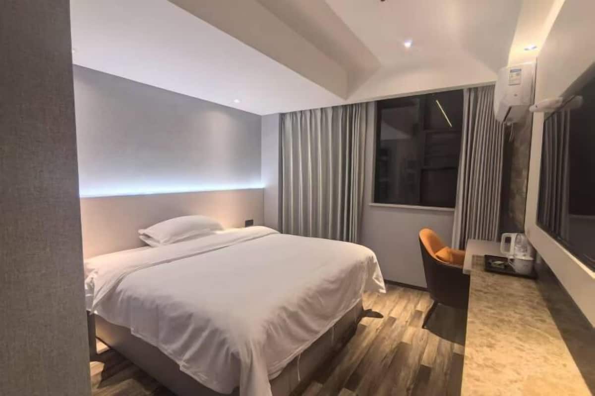 Una habitación de hotel moderna con cama, una silla, una mesita y una ventana con cortinas.