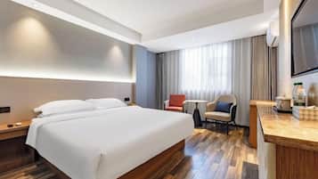 A hotel room with a large bed, a desk, a chair, and a TV.