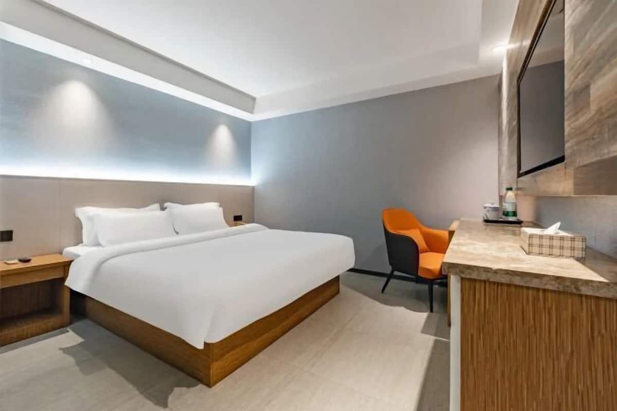 Una habitación de hotel moderna con una cama grande, una mesita de noche de madera, una pequeña mesa con una silla y un televisor montado en la pared.