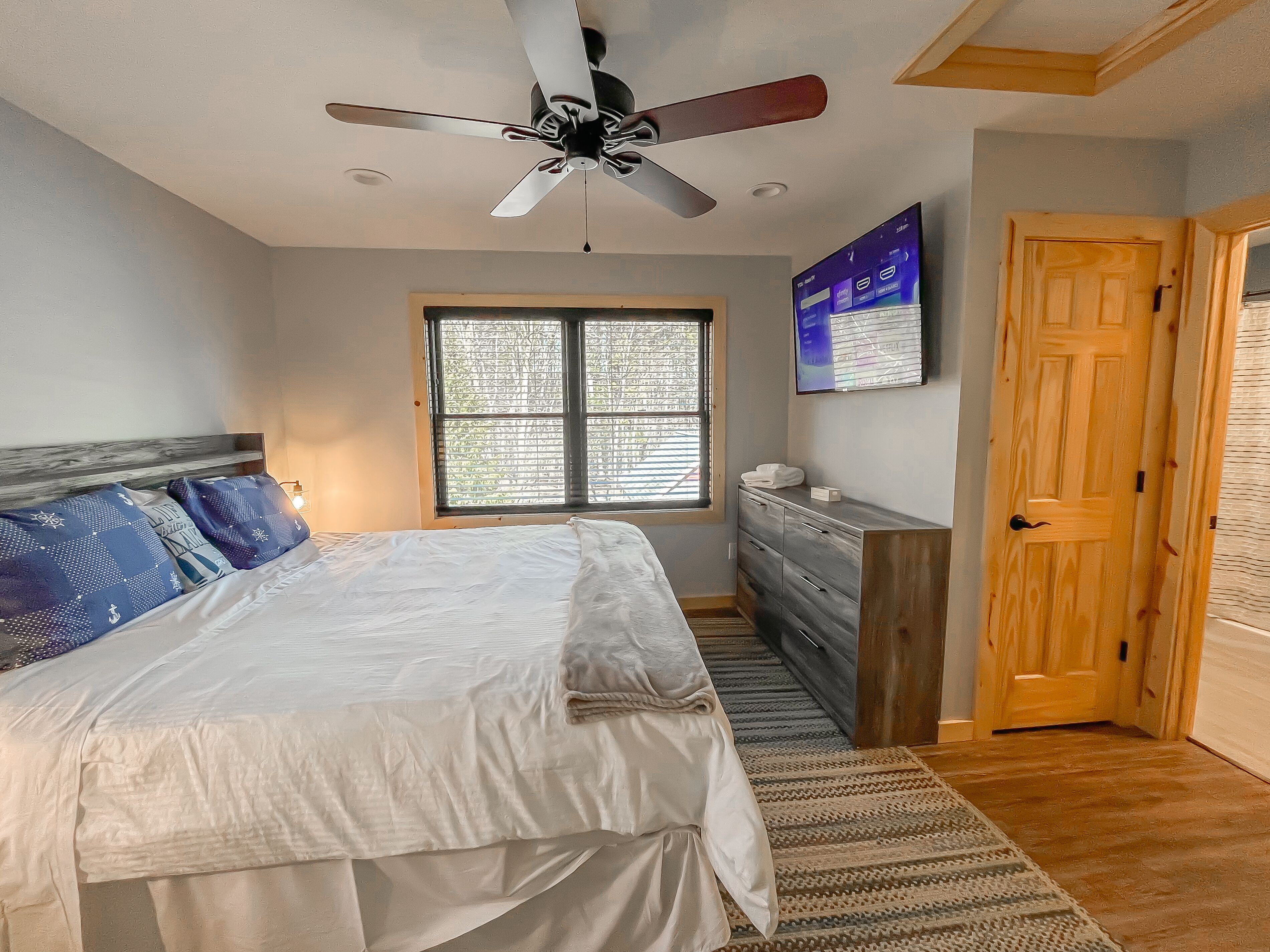 A bedroom with a bed, a dresser, a ceiling fan, a window, and a door.