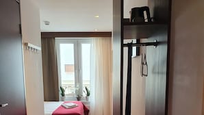 Habitación de hotel con cama, una mesita, ventana con cortinas, suelo de madera y perchero.