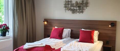Une chambre d’hôtel avec un lit en bois, une literie rouge, un élément décoratif mural et une fenêtre avec des rideaux.
