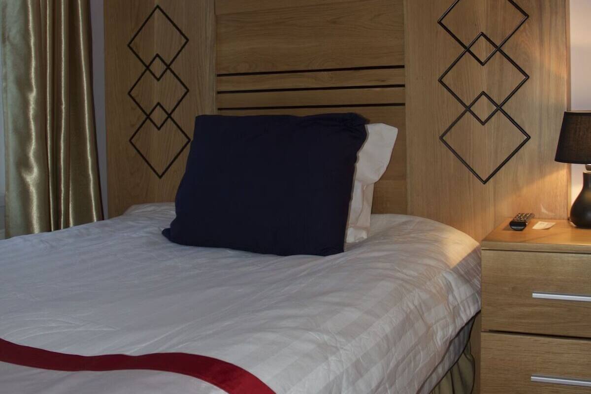A hotel room with a bed, a nightstand with a lamp, and a wooden headboard with geometric patterns.