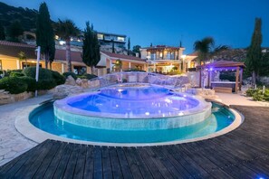 Un jacuzzi rond, entouré d’une terrasse en bois, avec en arrière-plan une colline et un bâtiment doté d’un balcon.
