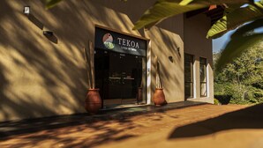 The exterior of a building named "TEKOA Lodge de Selva" with a modern design, large windows, and potted plants at the entrance.