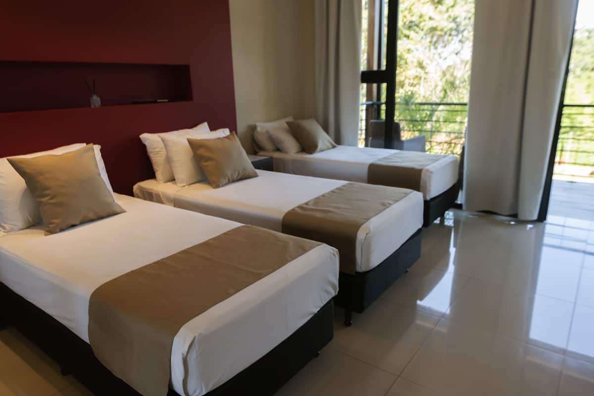 Habitación de hotel con dos camas, una pared de acento roja y vistas a zonas verdes.