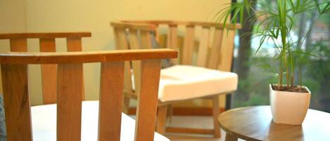 A wooden chair with a white cushion, another wooden chair in the background, and a small round table with a potted plant.