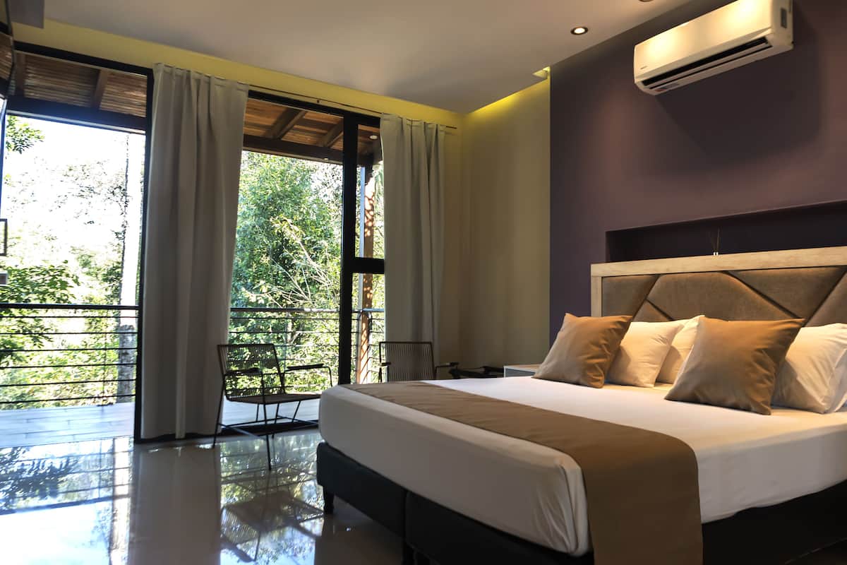 Un dormitorio moderno con una cama grande, un balcón con una silla y un equipo de aire acondicionado.