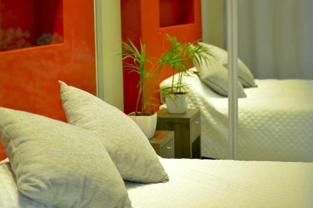 Habitación de hotel con dos camas, una planta en maceta y una pared roja decorativa.