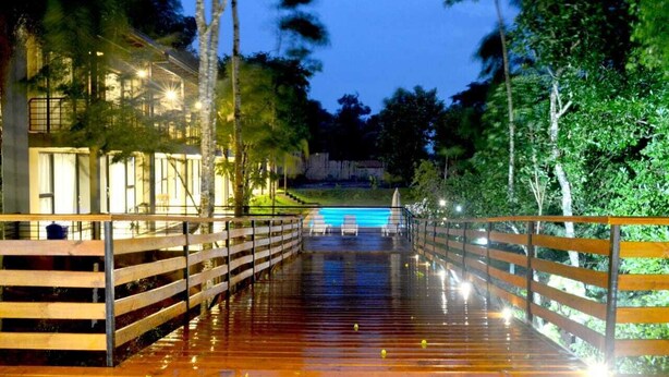 A wooden deck leading to a swimming pool with a view of a building and trees.