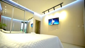 A modern bedroom with a large bed, a flat-screen TV mounted on the wall, and a mirror reflecting the room.