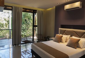 Una habitación de hotel moderna con una cama grande, un escritorio y un balcón con vistas a zonas verdes.