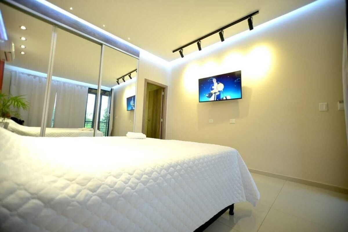 Un dormitorio moderno con una cama grande, un televisor montado en la pared y un espejo que refleja la habitación.