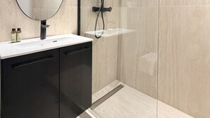 A modern bathroom with a glass shower enclosure, a round mirror, and a black cabinet.