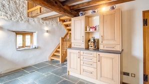 A rustic kitchen with stone flooring, wooden cabinets, and a stone wall.