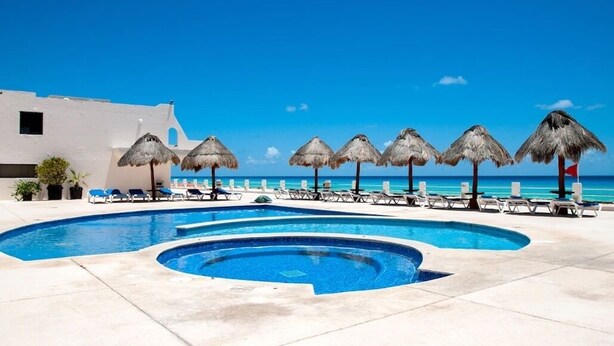 A swimming pool with lounge chairs and thatched umbrellas, a white building, and a clear blue sky. - Oceanfront 2BR Villa for 6 -  3 Bathrooms - Walk to La Isla & Beach (Cancún)