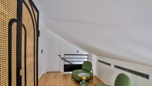Ein modernes Schlafzimmer im Loft-Stil mit schrägverdeckter Decke, einem grünen Polsterstuhl, einem kleinen runden Tisch und einem Bettgestell aus schwarzem Metall.