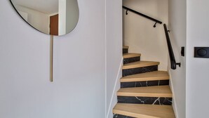 Eine moderne Treppe mit Holzbeschlägen und schwarzen Marmorstufen, einer schwarzen Handläufe und einem runden Spiegel an der Wand.