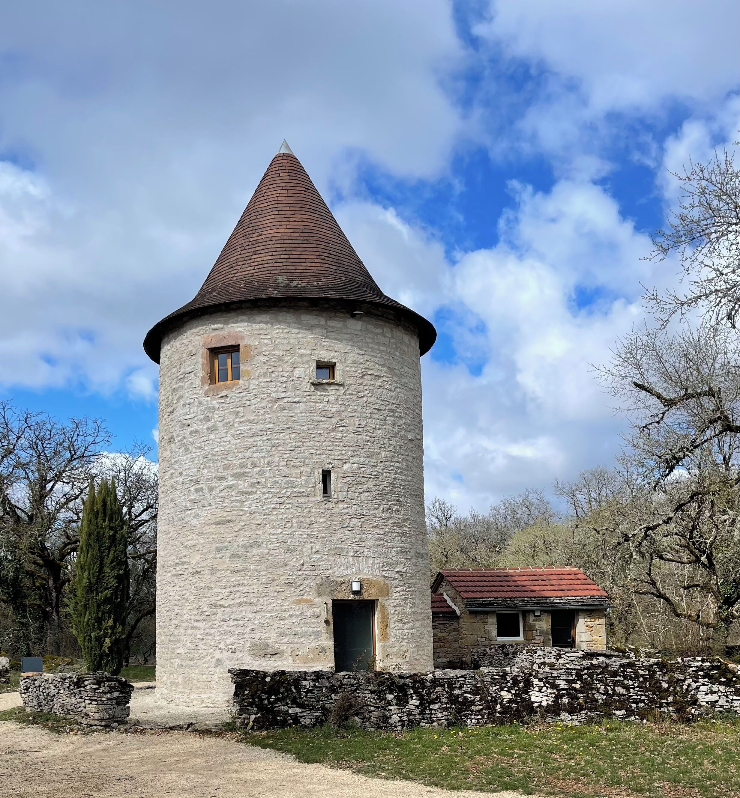 Une tour de pierre surmontée d’un toit conique, avec une petite porte et une fenêtre.