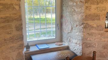 Une pièce rustique avec un banc en bois, une petite table et une fenêtre donnant sur un paysage verdoyant.