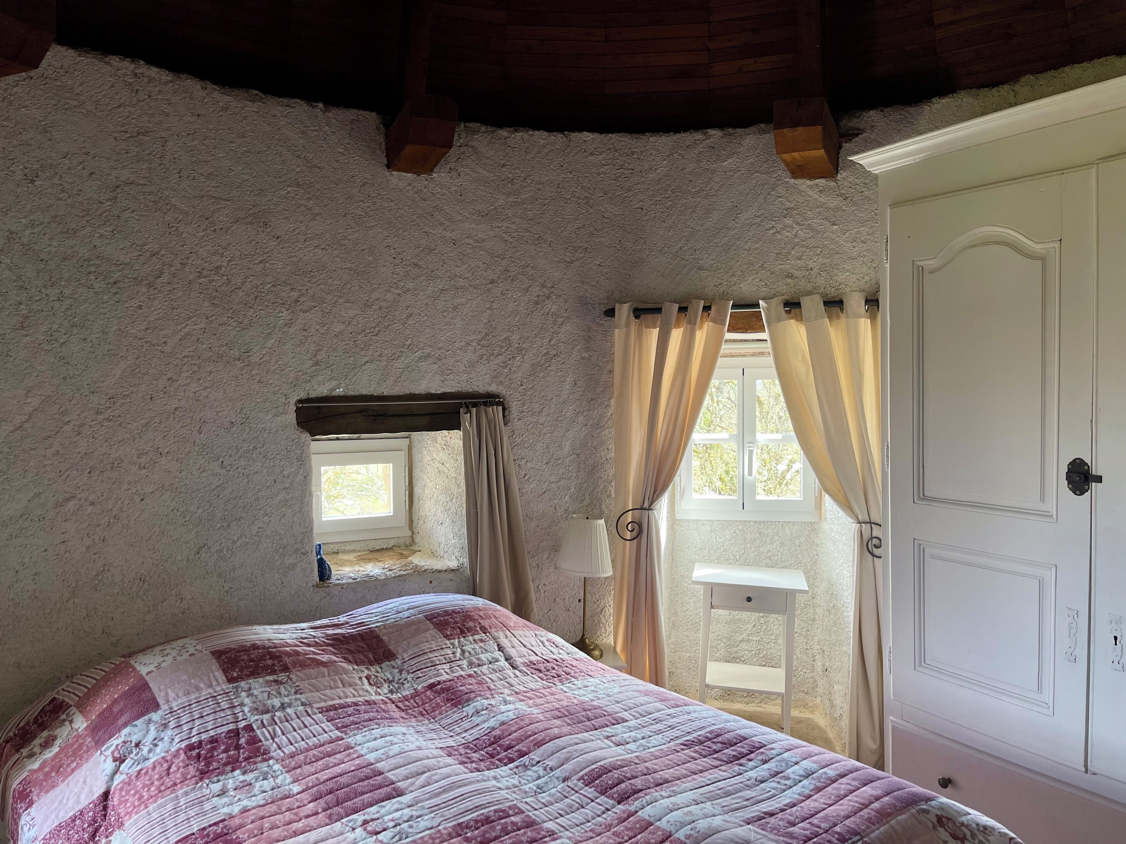 A bedroom with a bed, a window with curtains, a door, and a small window above the bed.