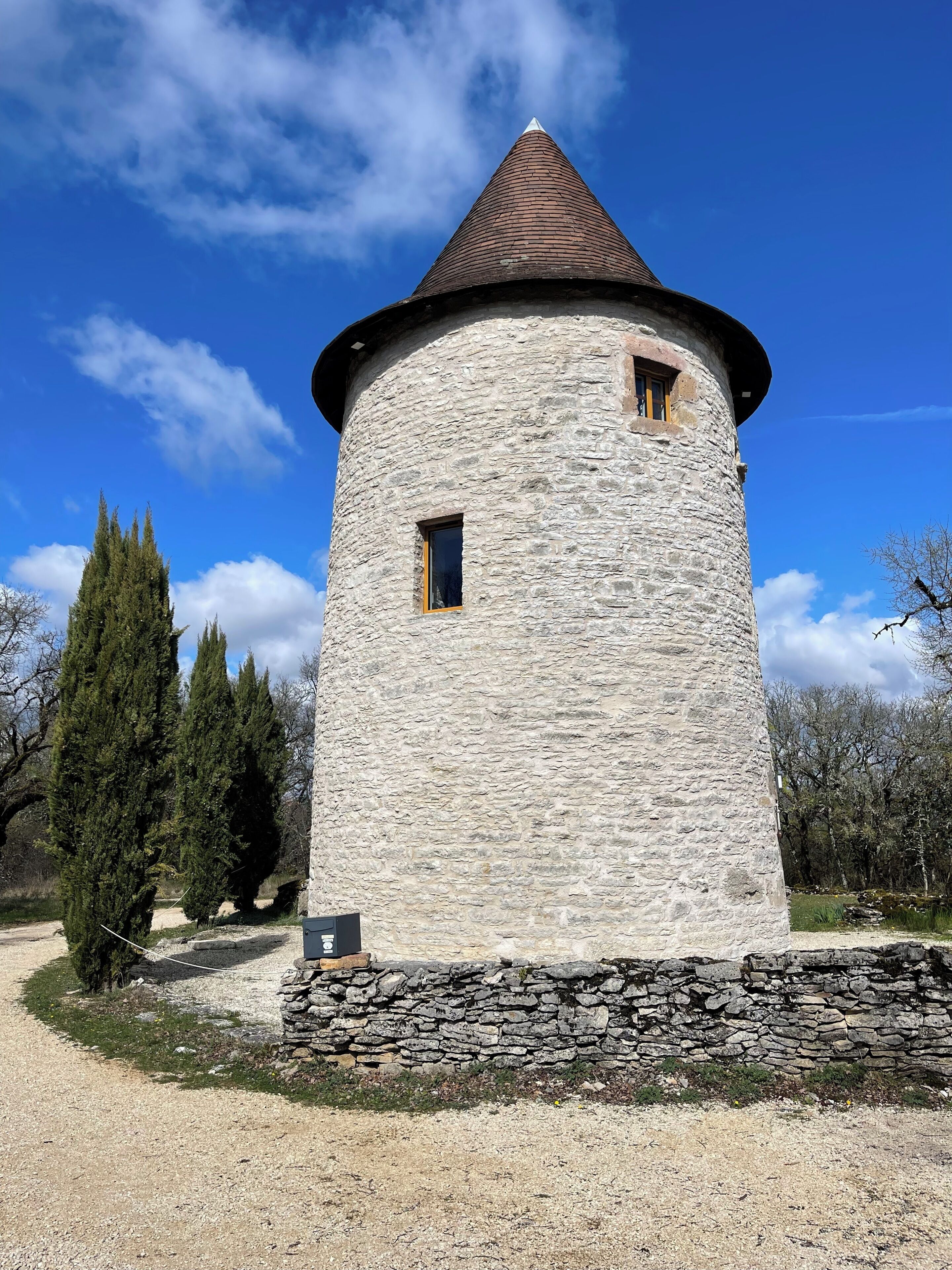 Une tour de pierre surmontée d’un toit conique, avec une petite fenêtre et un chemin de gravier menant à sa base.