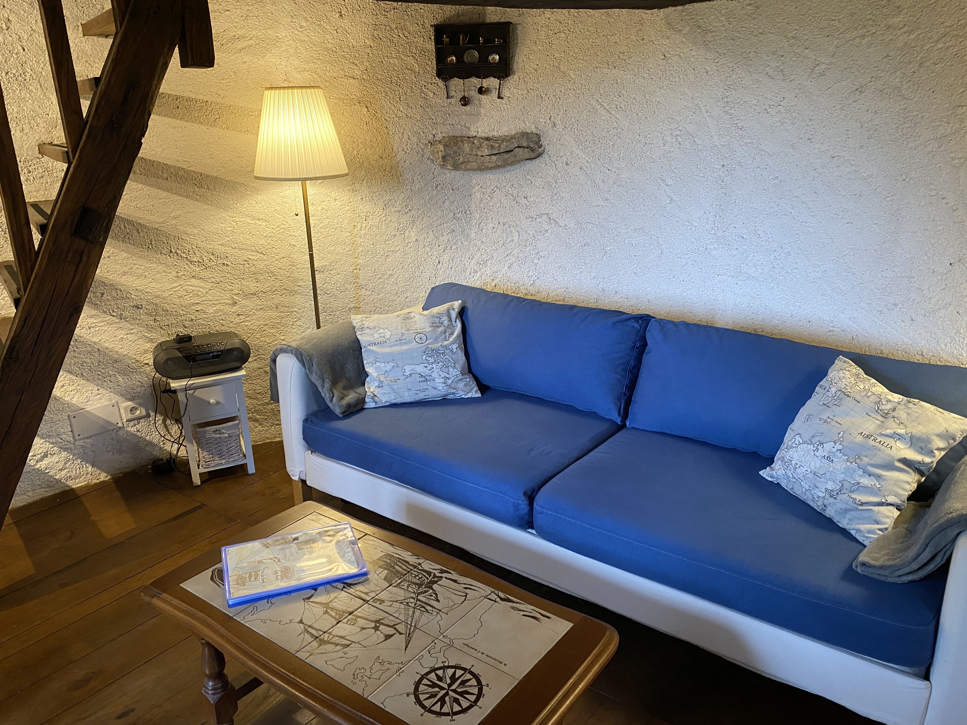 Een knusse woonkamer met een blauwe bank, een houten bijzettafeltje met een kaart, en een lamp.