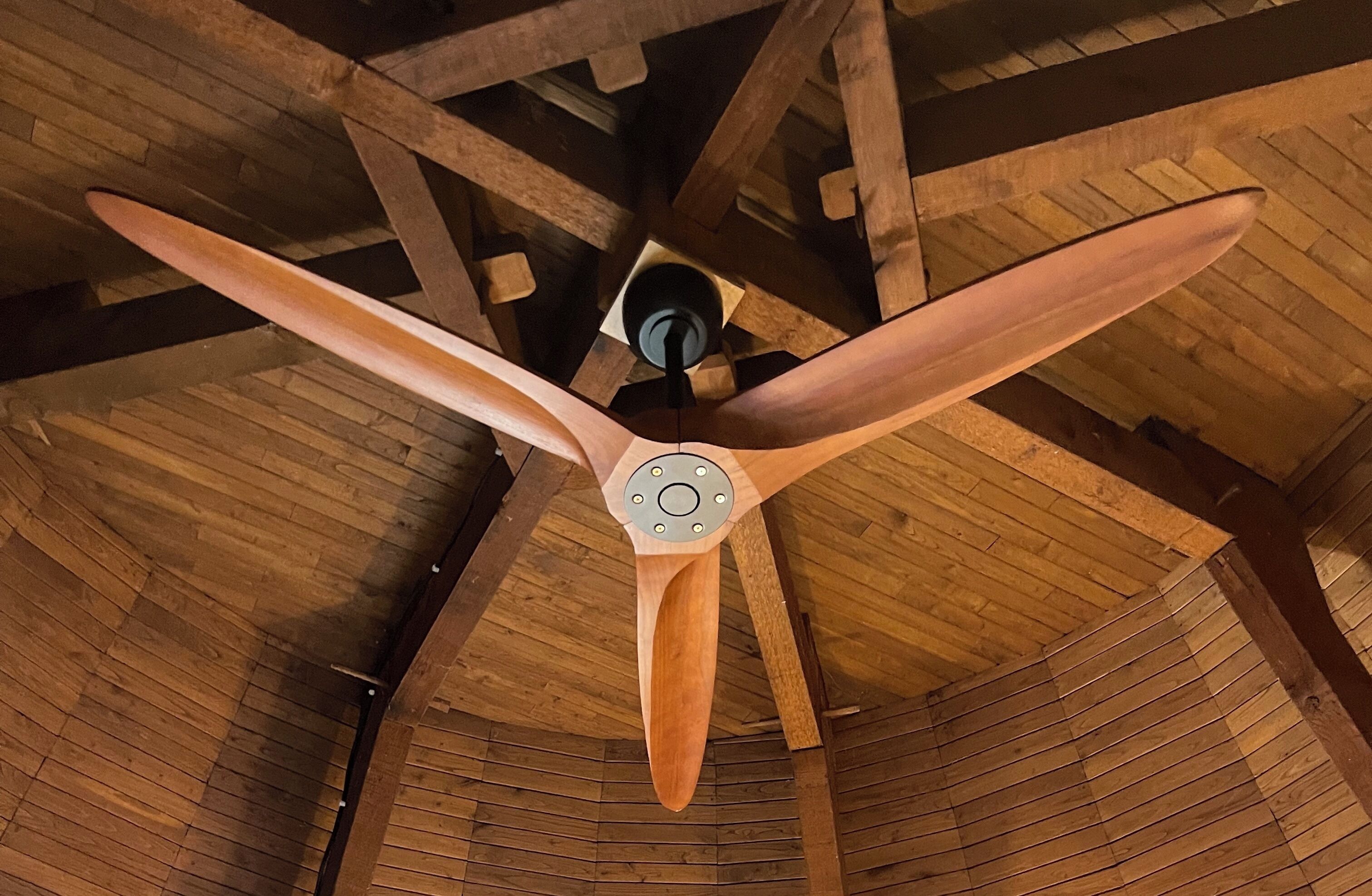 A ceiling fan with three blades in a wooden room with exposed beams.
