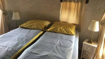 A bed with a blue and yellow bedspread, two pillows, a nightstand with a lamp, and a wall-mounted curtain.