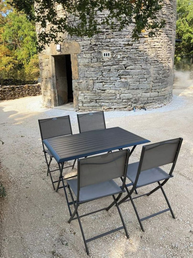 A stone building with a door, a table with four chairs, and a gravel ground.