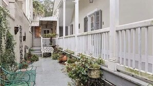 A narrow, white-walled corridor with a covered porch, potted plants, and a bench.