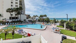 A hotel pool area with multiple swimming pools, lounge chairs, and palm trees. - OCEANFRONT condo directly overlooking the clear blue water of the Gulf of Mexico (Madeira Beach)