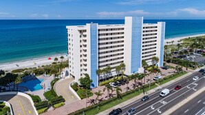 A multi-story hotel with a pool, located near a beach with palm trees and a clear blue sky. - OCEANFRONT condo directly overlooking the clear blue water of the Gulf of Mexico (Madeira Beach)