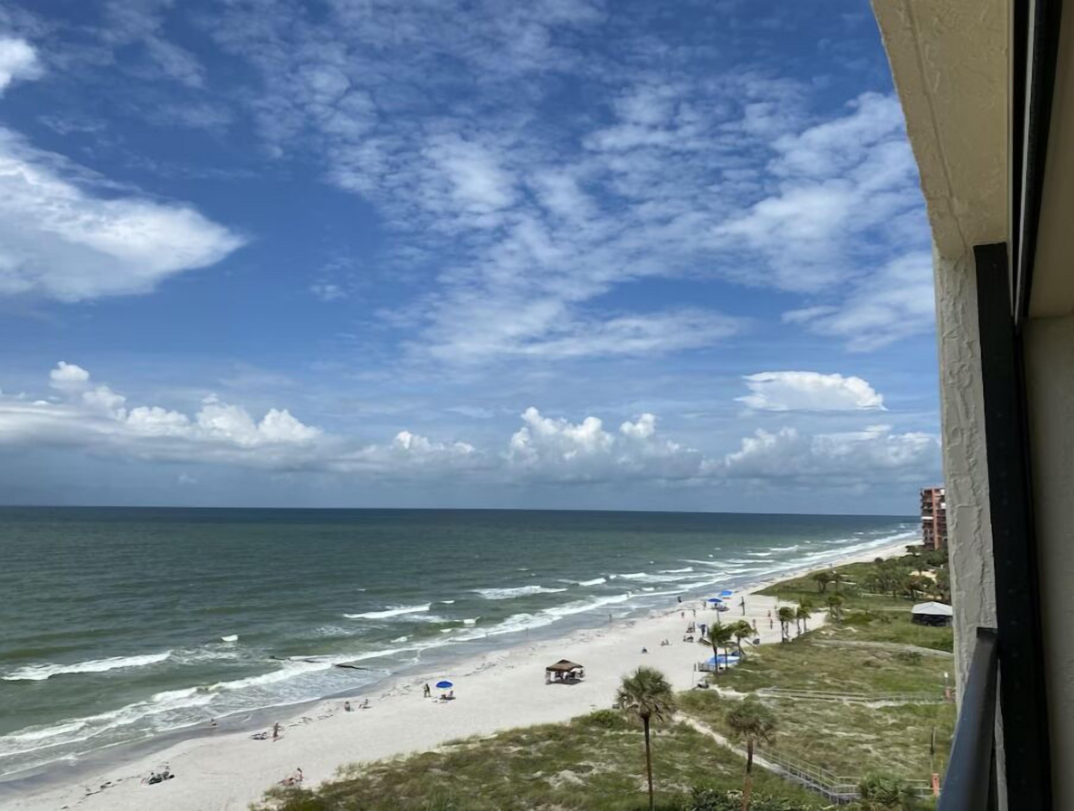 A beach view with a clear sky, ocean waves, and a few people on the sand.
