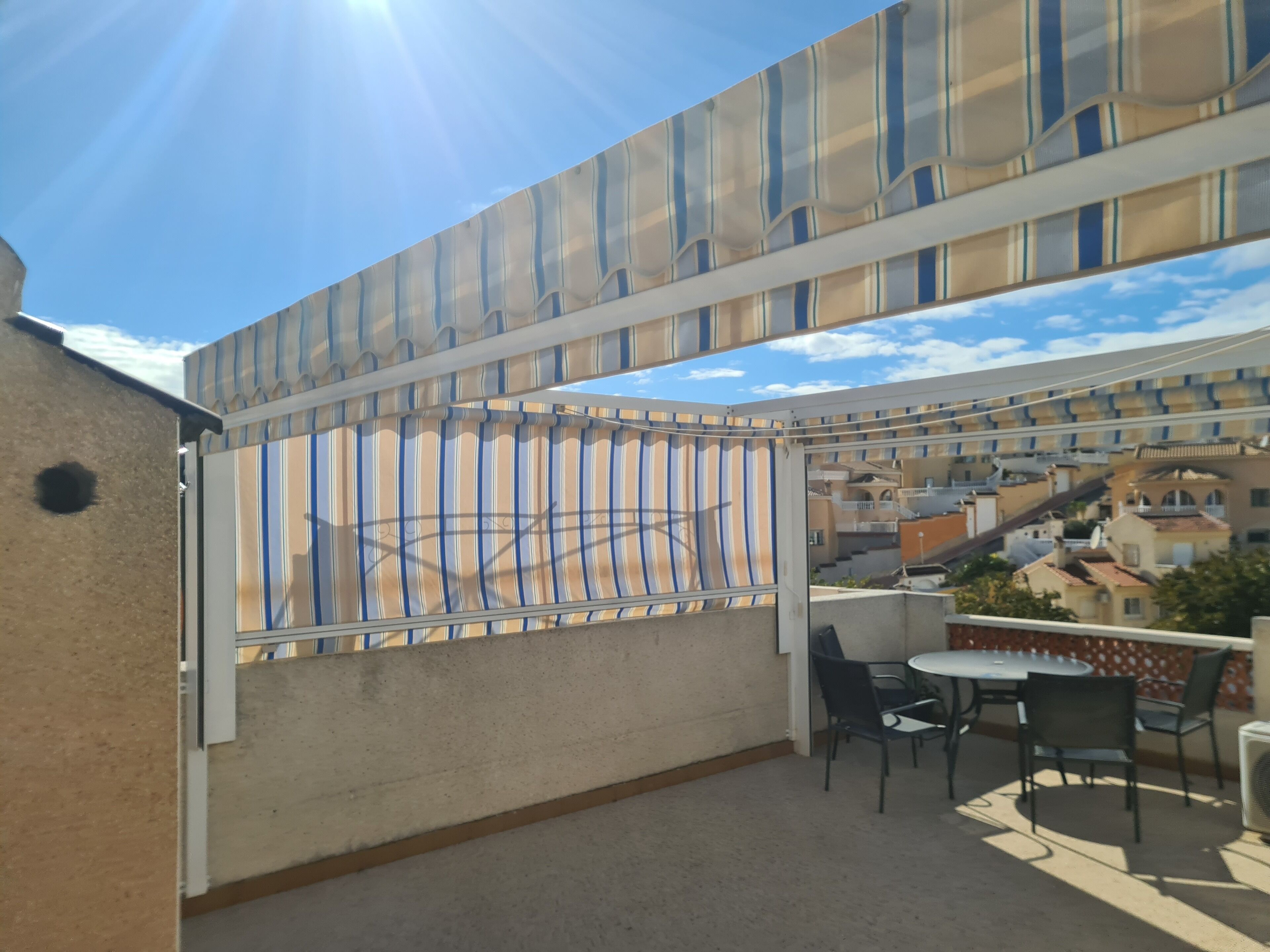 Un balcon agrémenté d’un auvent à rayures, avec des sièges d’extérieur, et une vue sur les bâtiments qui se dressent à l’arrière-plan.