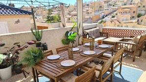 A wooden dining table set outdoors with chairs, surrounded by potted plants. - Gorgeous 3 Bed En-Suite, Huge Roof Terrace overlooking Pool and La Marquesa Golf (Ciudad Quesada)