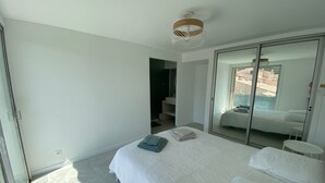 A bedroom with a large bed, a wardrobe with a sliding door, and a view of the outside through the door. - Le Cosy Beach (Saint-Cyr-sur-Mer)