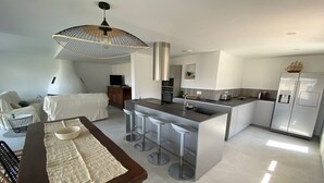 A modern kitchen with a central island, bar stools, a dining table with a placemat, and a hanging light fixture. - Le Cosy Beach (Saint-Cyr-sur-Mer)