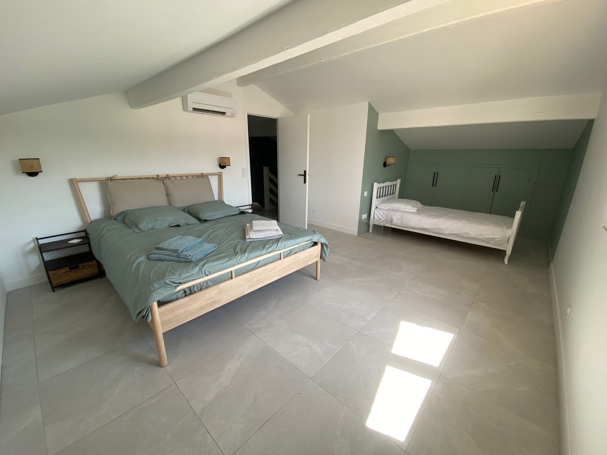 A bedroom with a large bed, a smaller bed, a wardrobe, and a bedside table.
