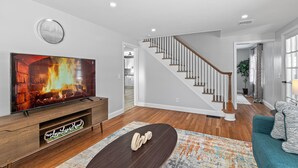 Una sala de estar moderna con un televisor de pantalla plana, un mueble de entretenimiento de madera y una escalera que sube a un nivel superior.