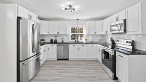 Una cocina moderna con armarios blancos, electrodomésticos de acero inoxidable y una encimera negra.