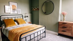 Un dormitorio con estructura metálica para la cama, cómoda de madera, espejo y obras de arte en la pared.