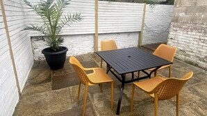 Un patio con una mesa, sillas, una planta en maceta y una pared de ladrillo.