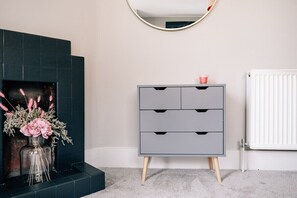 A room with a grey dresser, a mirror, and a fireplace with flowers.