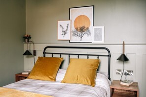 A bed with two pillows, a bedside table with a lamp, and framed artwork on the wall.
